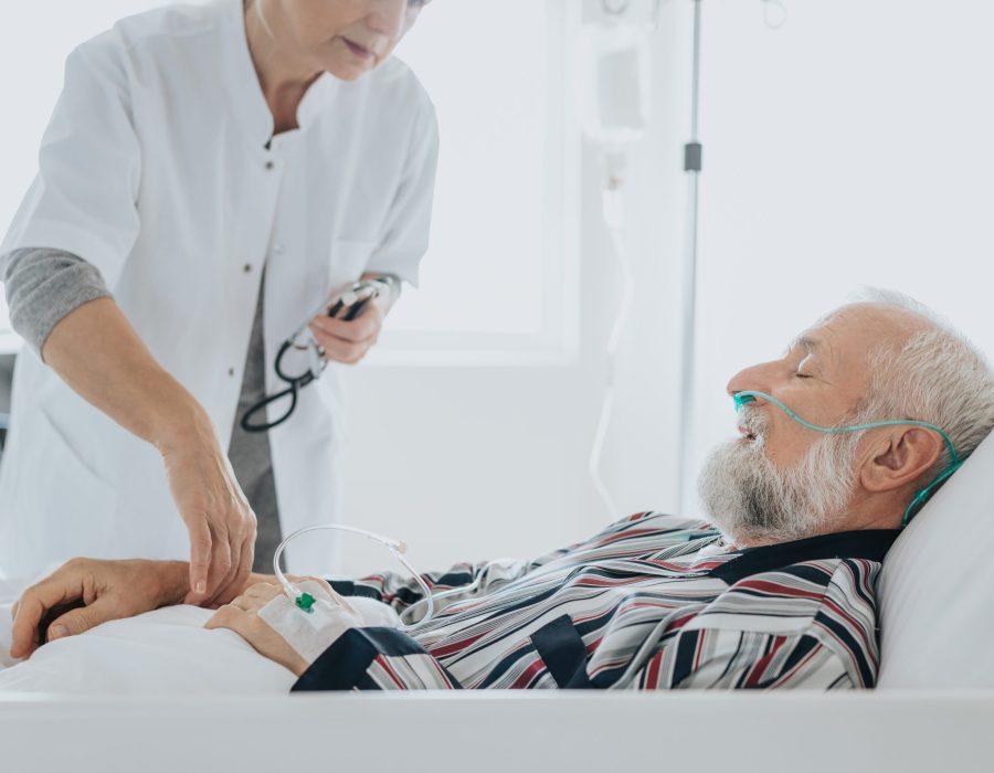 Doctor checking the pulse at sick older patient in a hospital bed